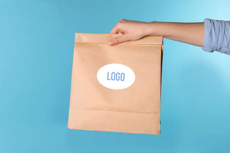 Woman holding paper bag with logo on light blue background, closeup