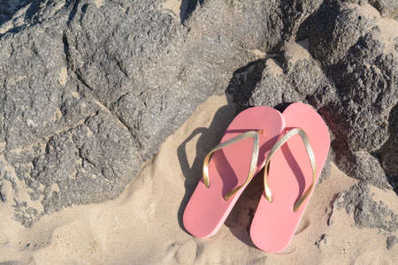 Stylish pink flip flops on sandy beach near rocks, flat layの写真素材