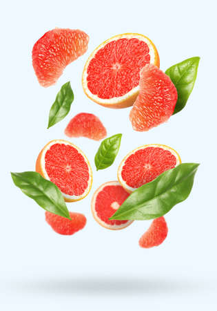 Tasty ripe grapefruits and green leaves falling on light backgroundの写真素材