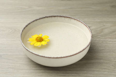 Beige bowl with water and yellow flower on wooden table, closeupの写真素材