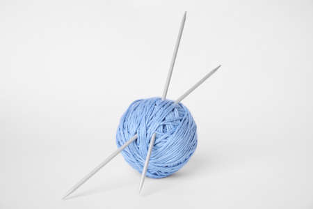 Soft light blue woolen yarn and knitting needles on white background