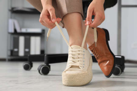 Woman taking off uncomfortable shoes and putting on sneakers in office, closeupの写真素材