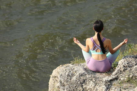 Young woman meditating on cliff near river, back view. Space for textの写真素材