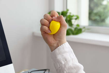 Man squeezing yellow stress ball in office, closeupの写真素材