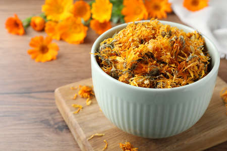 Bowl of dry calendula flowers on wooden table. Space for textの写真素材