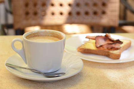 Cup of coffee and delicious sandwich with fried bacon on beige tableの写真素材