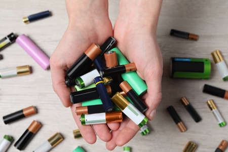 Woman holding many used electric batteries in her hands over white table, closeupの写真素材