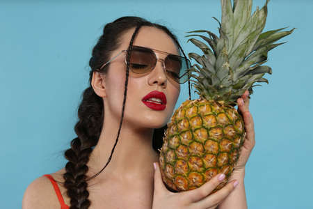 Young woman with fresh pineapple on light blue background. exotic fruitsの写真素材