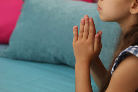 Cute little girl with hands clasped together praying on bed, closeup. Space for textの写真素材