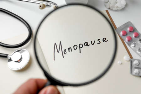 Woman holding magnifying glass over notebook with word Menopause, closeupの写真素材