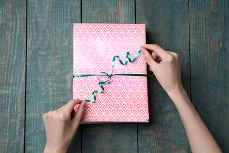 Woman wrapping gift with beautiful paper and ribbon at light blue wooden table, top view