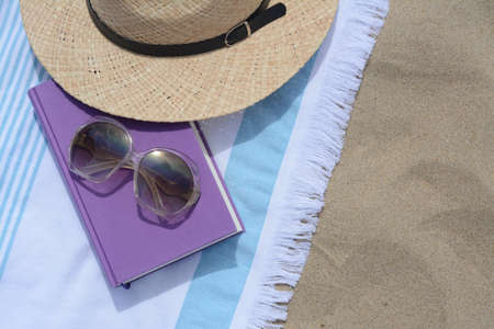 Beach towel with book, sunglasses and straw hat on sand, flat lay. Space for textの写真素材