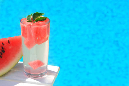 Refreshing watermelon drink in glass near swimming pool outdoors. Space for textの写真素材