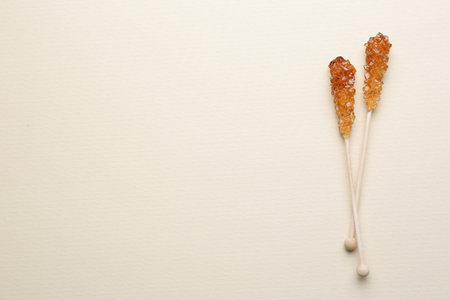 Wooden sticks with sugar crystals and space for text on beige background, flat lay. Tasty rock candiesの写真素材