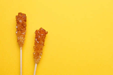 Wooden sticks with sugar crystals and space for text on yellow background, flat lay. Tasty rock candiesの写真素材