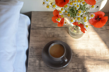 Beautiful bouquet of poppies and chamomiles near cup with coffee indoors, focus on flowersの写真素材