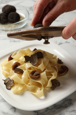 Woman slicing truffle onto tagliatelle at white marble table, closeupの写真素材