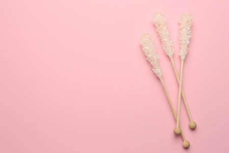 Wooden sticks with sugar crystals and space for text on pink background, flat lay. Tasty rock candiesの写真素材