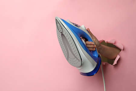 Woman holding modern iron through hole in pink paper, closeup. Space for textの写真素材