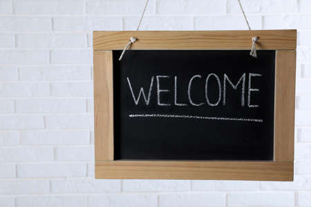 Small chalkboard with word Welcome hanging near white brick wall. Space for textの写真素材