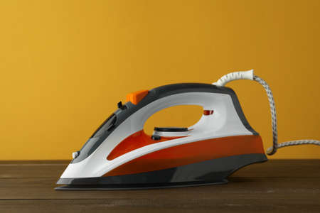 One modern iron on wooden table against orange background. home appliances