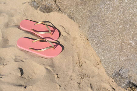 Stylish pink flip flops on sandy beach near rockの写真素材