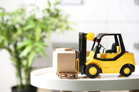 Toy forklift with cardboard box on table against blurred background. Courier serviceの写真素材