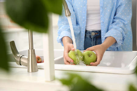 Woman washing fresh green apples in kitchen sink, closeupの写真素材