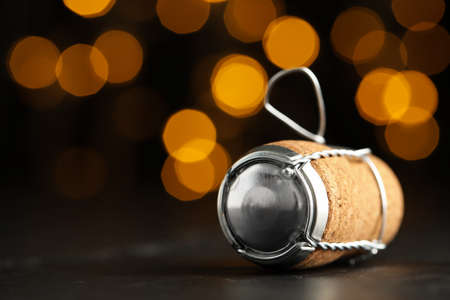 Sparkling wine cork with muselet cap on black table against blurred festive lights, closeup. Space for textの写真素材