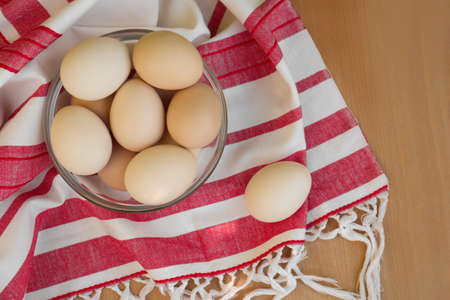 Fresh raw eggs and towel on wooden table, flat lay