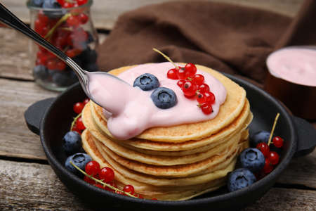 Tasty pancakes with natural yogurt, blueberries and red currants on wooden tableの写真素材