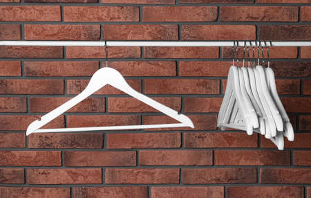 White clothes hangers on rail near red brick wallの写真素材