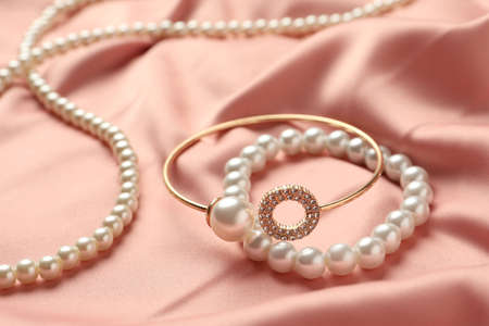 Elegant necklace and bracelets with pearls on pink silk, closeupの写真素材