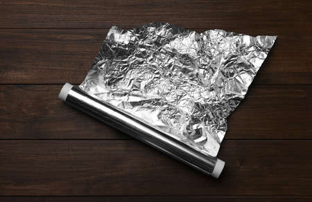 Roll of foil paper on wooden table, top view