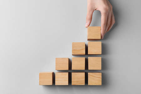 Woman holding wooden cube near others on light background, top view. management concept