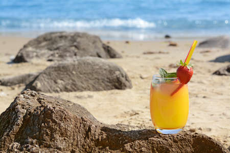Glass of refreshing drink with strawberry on beach near sea, space for textの写真素材