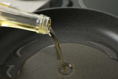 Pouring cooking oil from bottle into frying pan, closeup