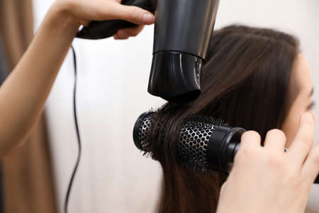 Stylist drying client's hair in beauty salon, closeup