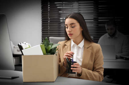 Dismissed woman packing personal stuff into box in officeの写真素材