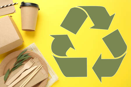 Flat lay composition with eco friendly tableware and recycling symbol on yellow background