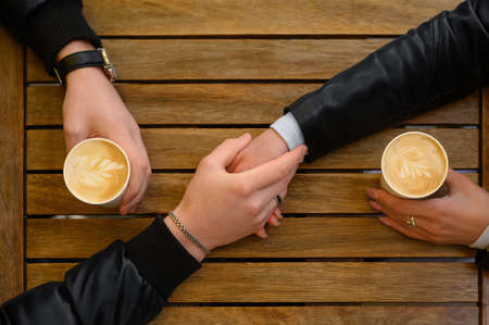 Lovely couple with coffee holding hands together at wooden table, top view. romantic dateの写真素材