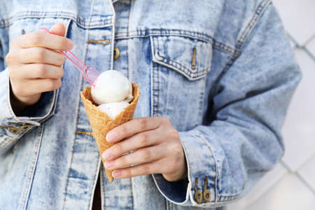Woman eating delicious ice cream on light background, closeup