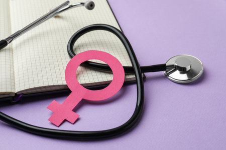 Female gender sign, open notebook and stethoscope on violet background, closeup. Women's health conceptの写真素材