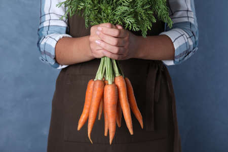 Woman holding ripe carrots on blue background, closeupの写真素材