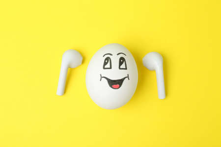 Egg with drawn happy face and earbuds on yellow background, flat layの写真素材