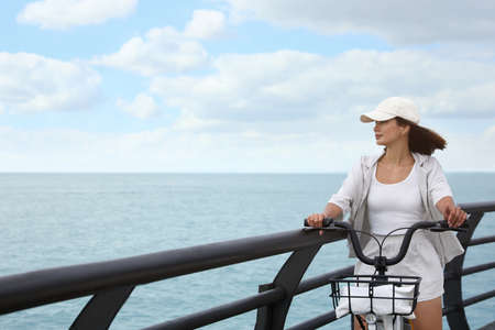 Beautiful young woman with bicycle near the sea. Space for textの写真素材