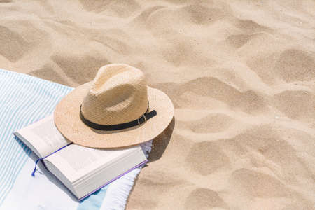 Beach towel with straw hat and book on sand. Space for textの写真素材