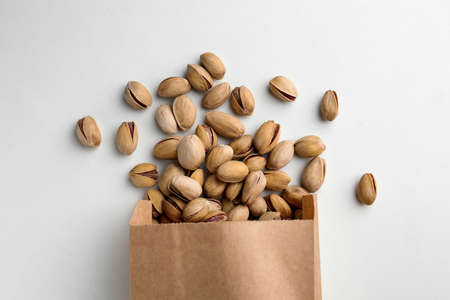 Overturned paper bag with pistachio nuts on white background, flat layの写真素材