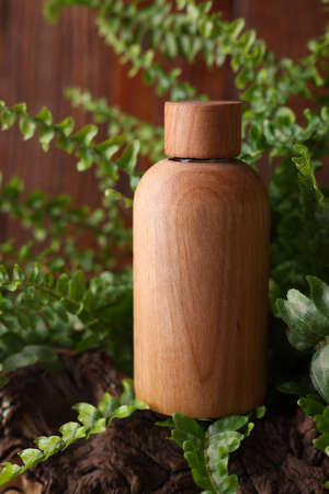 Wooden bottle of cosmetic product and green leaves on table, closeupの写真素材