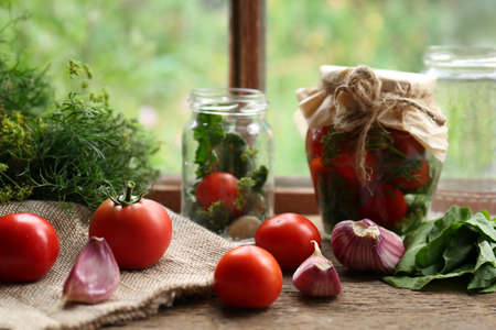 Glass jars, fresh vegetables and herbs on wooden table indoors. pickling recipeの写真素材